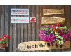 Mohnwirtin Maria mit Blumen und Schildern vor Holzwand in Österreich
